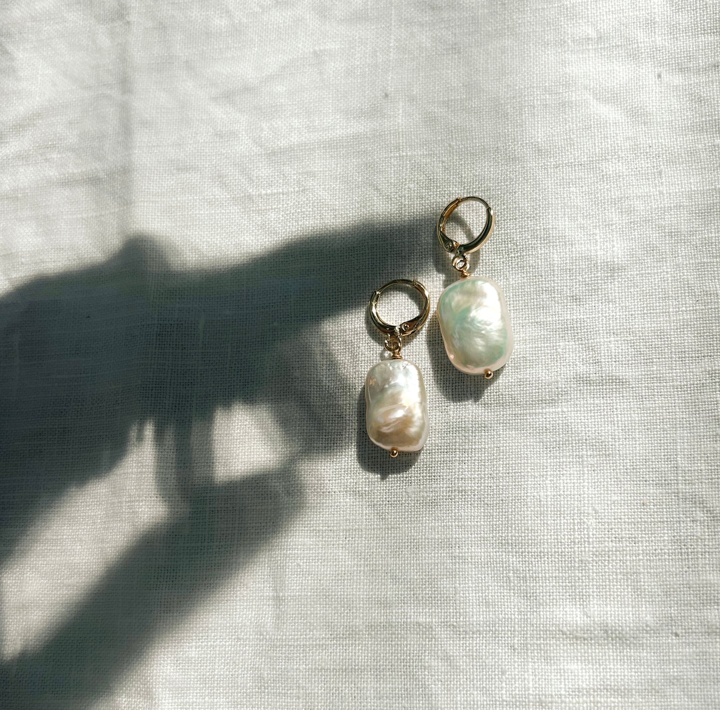 Gold Pearl huggies earrings flat lay on linen cloth